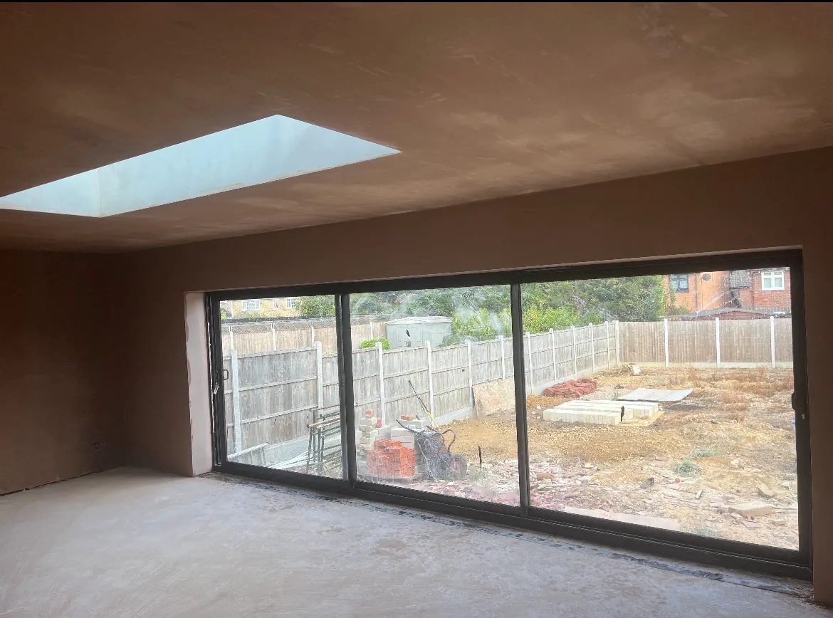 Freshly plastered extension interior with a skylight and wide black-framed glazing